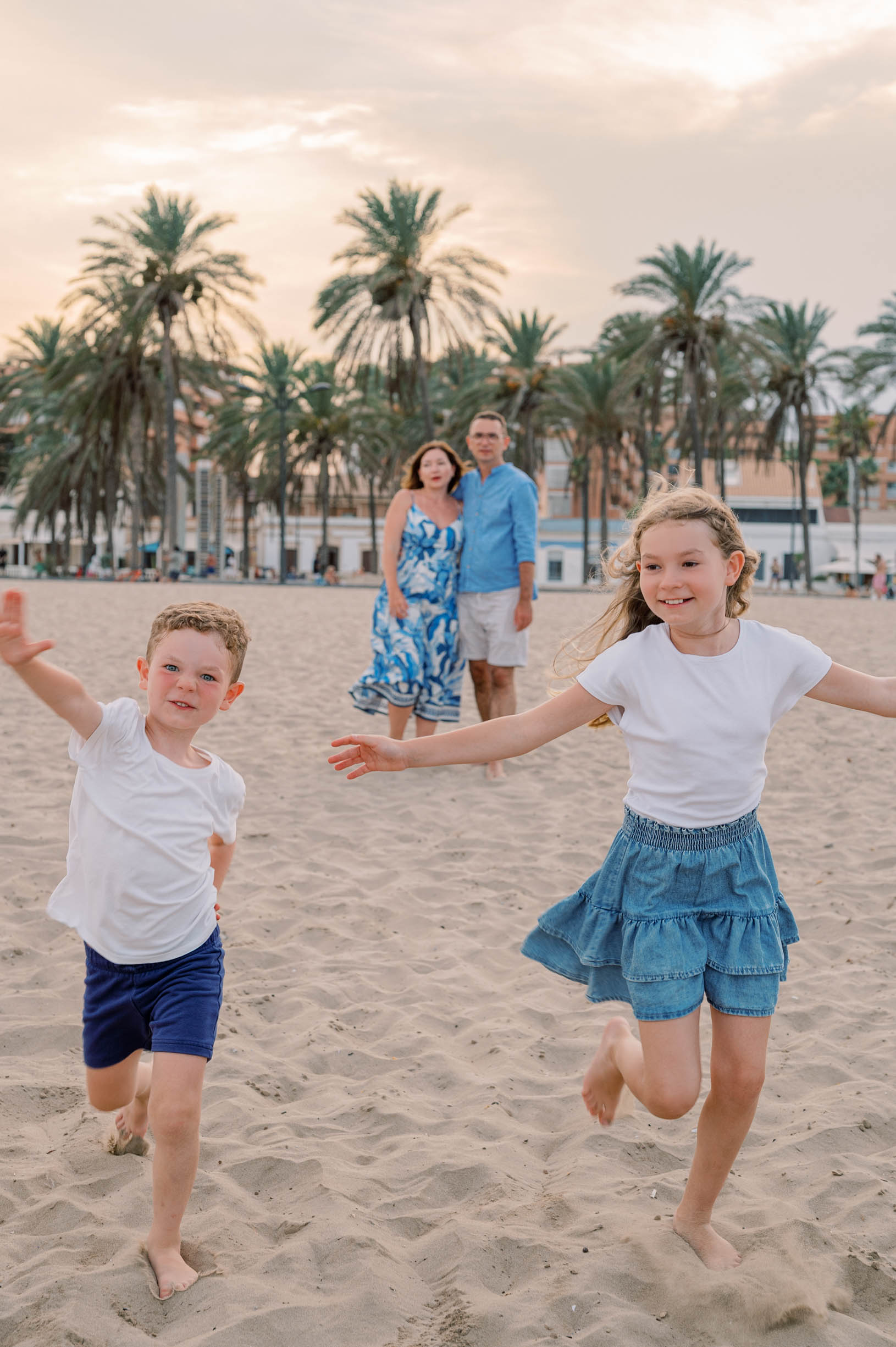 Two children running on Patacona Beach while their parents watch during a sunset family photoshoot in Valencia